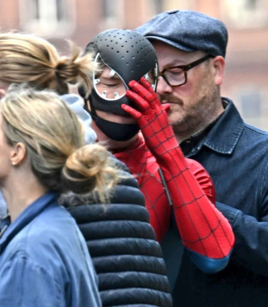 A new set photo from Spider-Man: Brand New Day shows Tom Holland in his Spider-Man suit wearing a black protective face mask, likely used between takes or before putting on the actual mask.