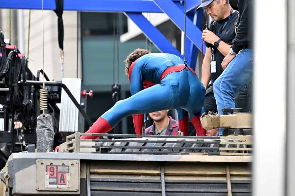 A new set photo from Spider-Man: Brand New Day shows Tom Holland in his Spider-Man suit wearing a black protective face mask, likely used between takes or before putting on the actual mask.