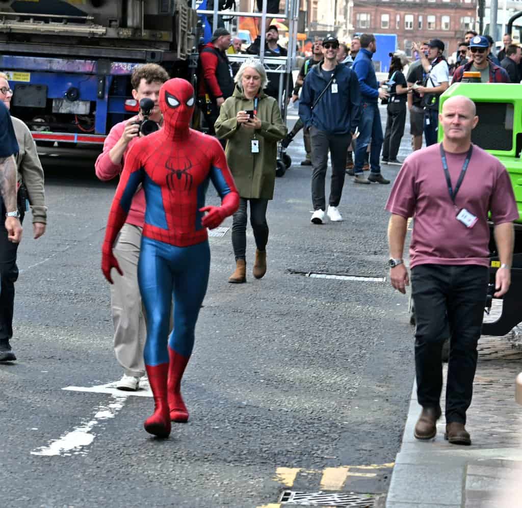 A new set photo from Spider-Man: Brand New Day shows Tom Holland in his Spider-Man suit wearing a black protective face mask, likely used between takes or before putting on the actual mask.